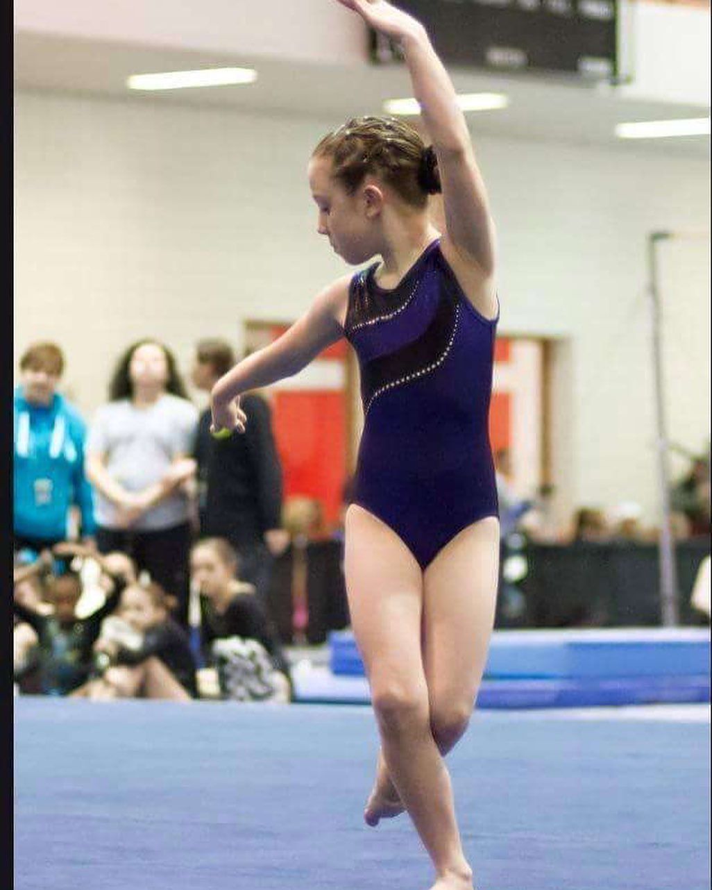 A girl in a blue leotard is doing a trick on a blue mat