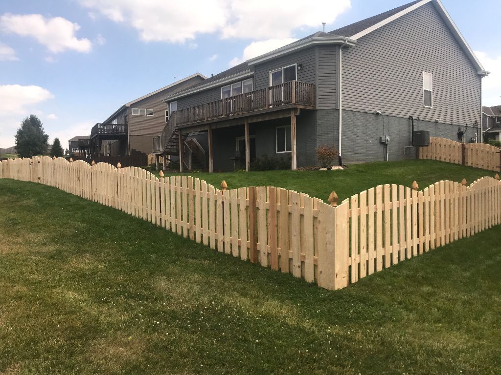 A wooden picket fence surrounds a lush green yard in front of a house.