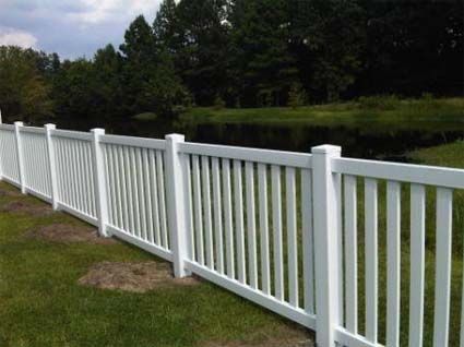 A white fence surrounds a grassy field with trees in the background.