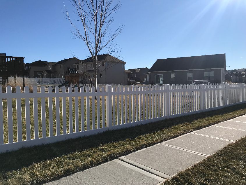 A white picket fence along a sidewalk in front of a house.