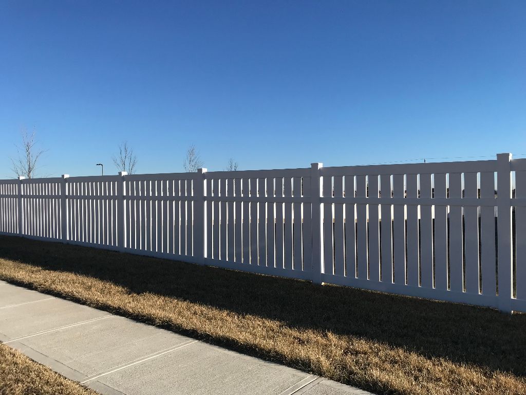 A white picket fence along a sidewalk with a blue sky in the background
