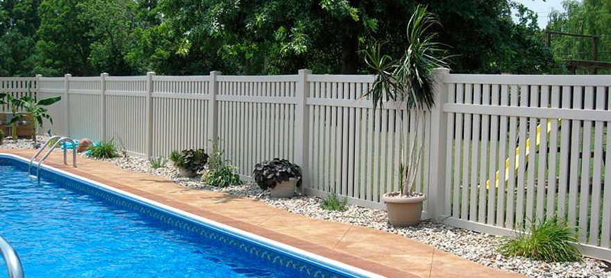 A white fence surrounds a large swimming pool.