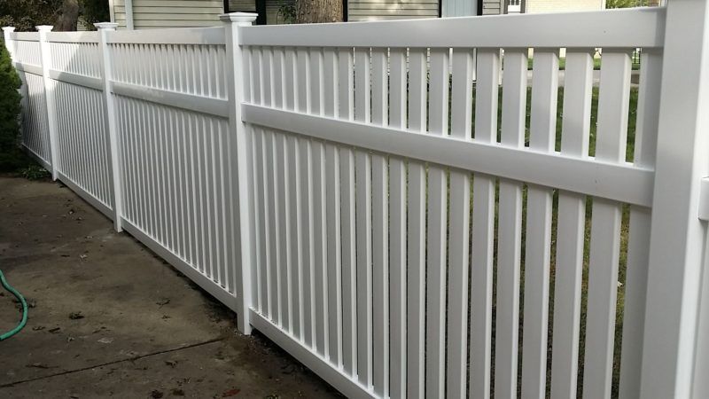 A white fence is sitting on a sidewalk next to a house.
