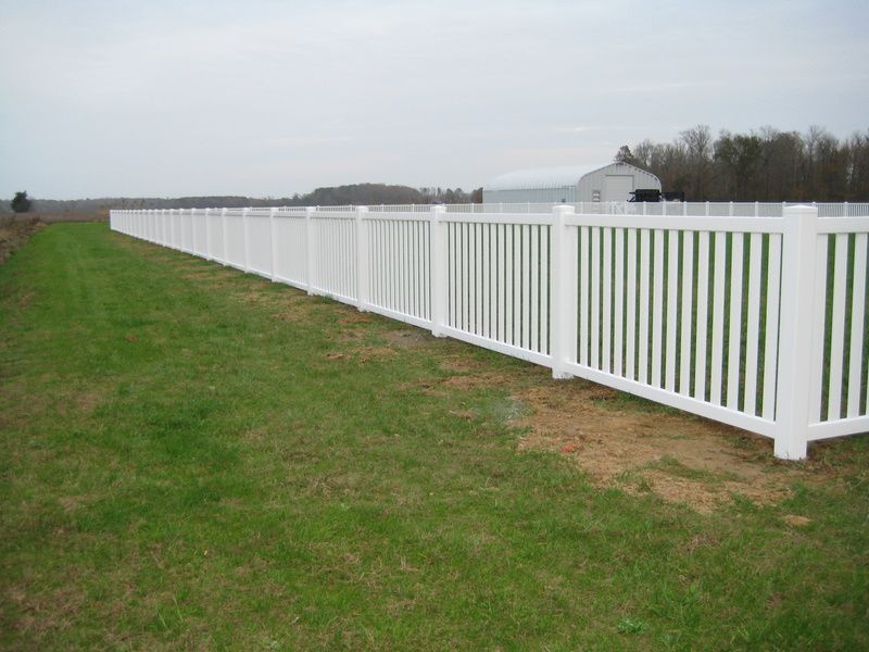 A long white fence surrounds a lush green field.