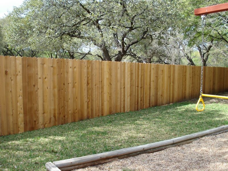 A wooden fence surrounds a playground with trees in the background.