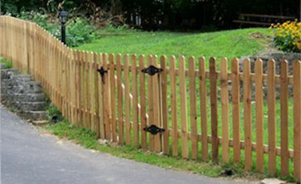 A wooden picket fence is along the side of a road.