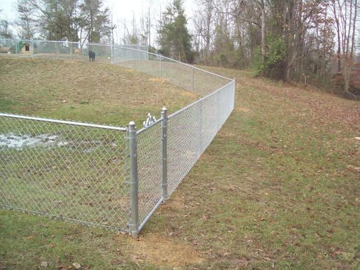 A chain link fence is in the middle of a grassy field.
