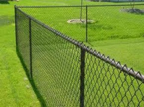 A chain link fence surrounds a lush green field.