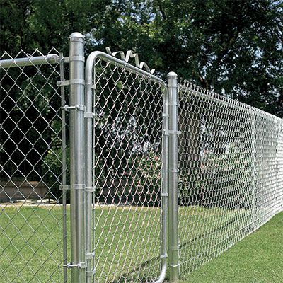 A chain link fence with a gate in the middle of a grassy field.