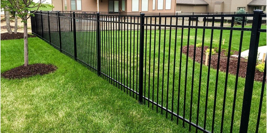 A black metal fence surrounds a lush green lawn in front of a house.