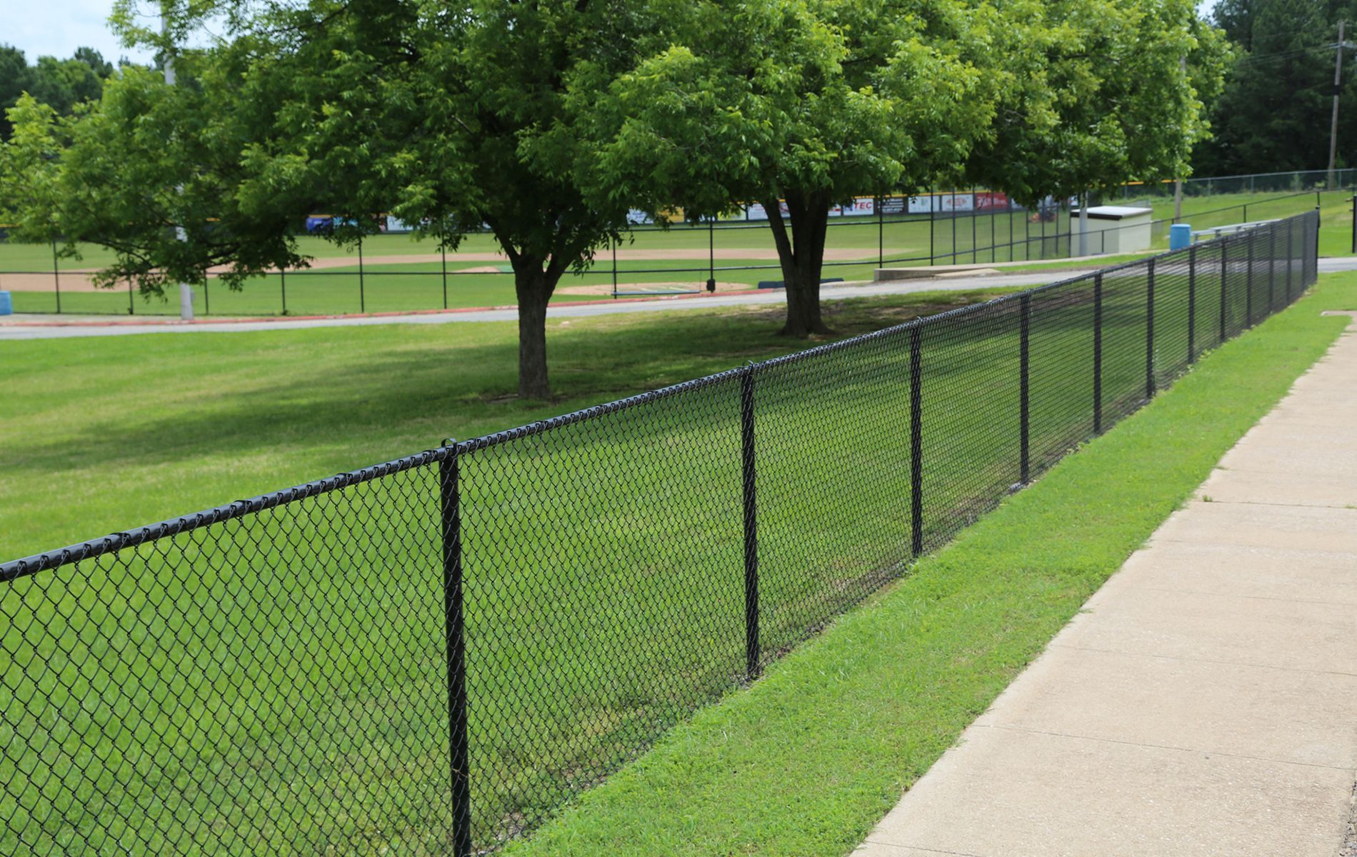 A chain link fence along a sidewalk in a park