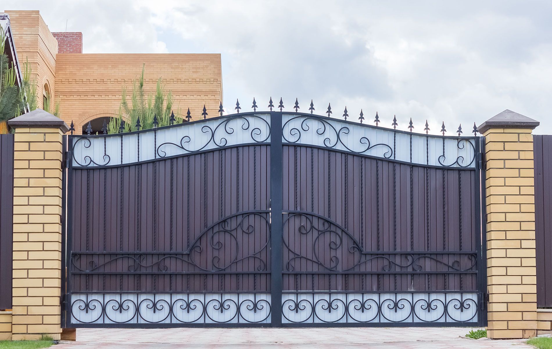 A wrought iron gate with a brick pillar in front of a house.