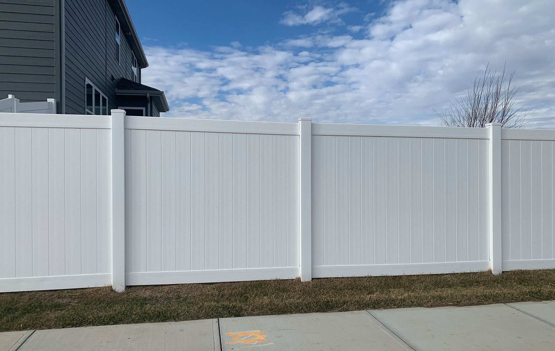 A white vinyl fence is sitting next to a sidewalk in front of a house.