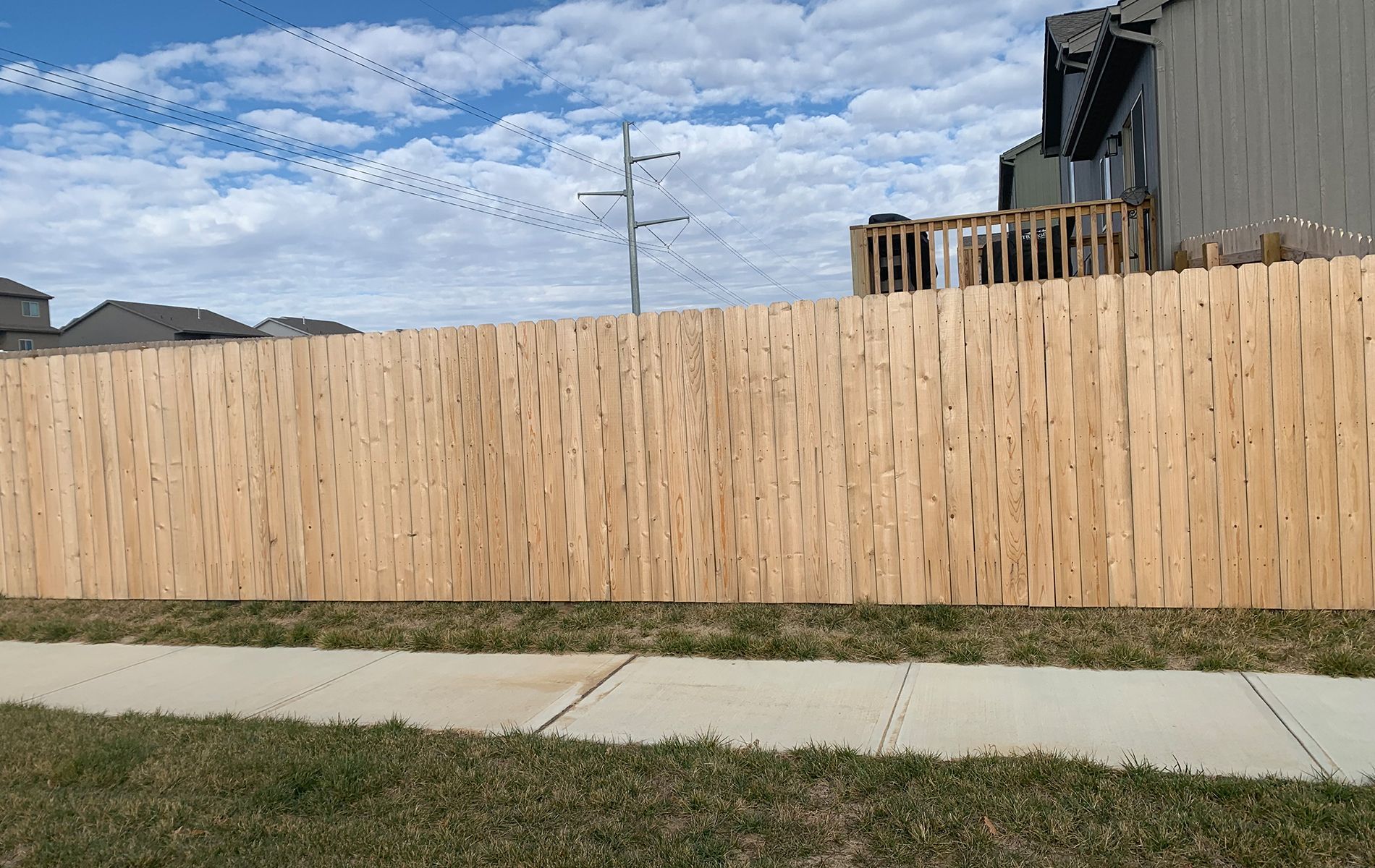 A wooden fence is sitting next to a sidewalk in front of a house.