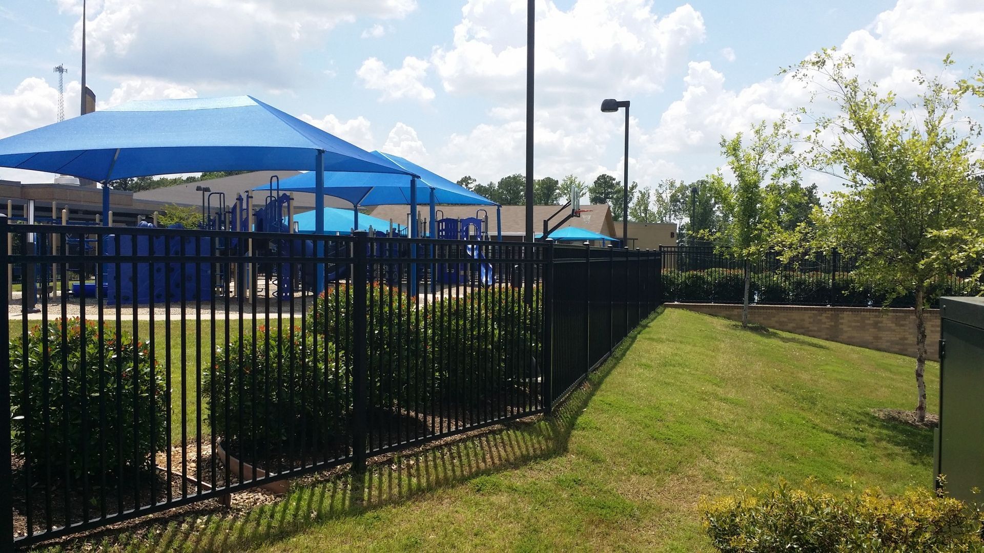A black fence surrounds a playground with blue umbrellas.