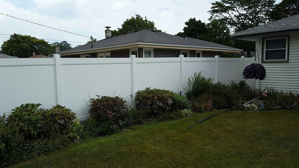 A white fence surrounds a lush green yard in front of a house.