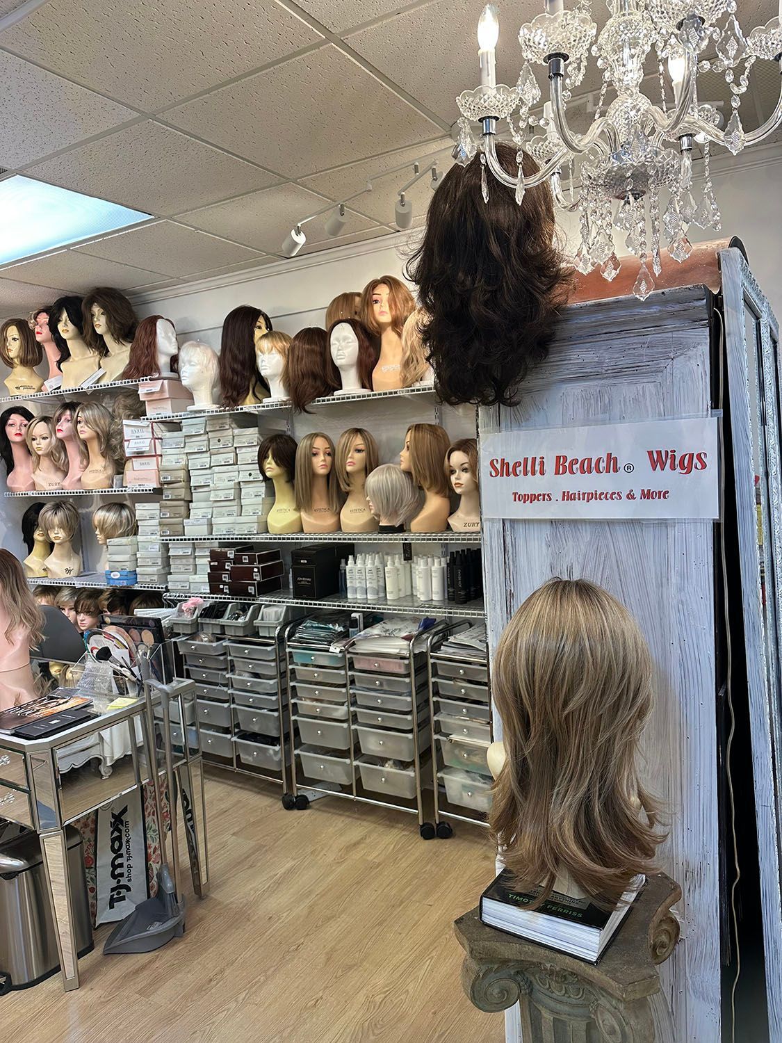Wig store aisle with mannequin heads, stacked trays, and a chandelier overhead.