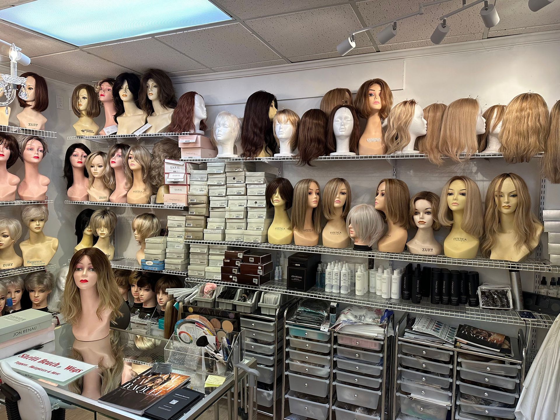 Wig shop display with rows of mannequin heads, assorted wigs, and stacked hair product boxes.