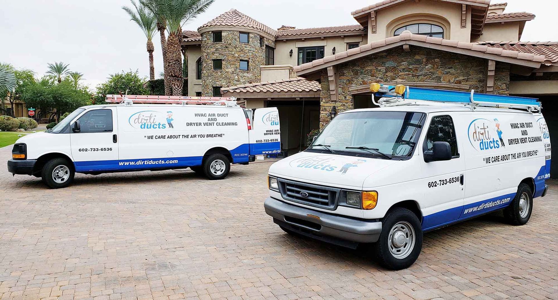 Two vans are parked in front of a large house.