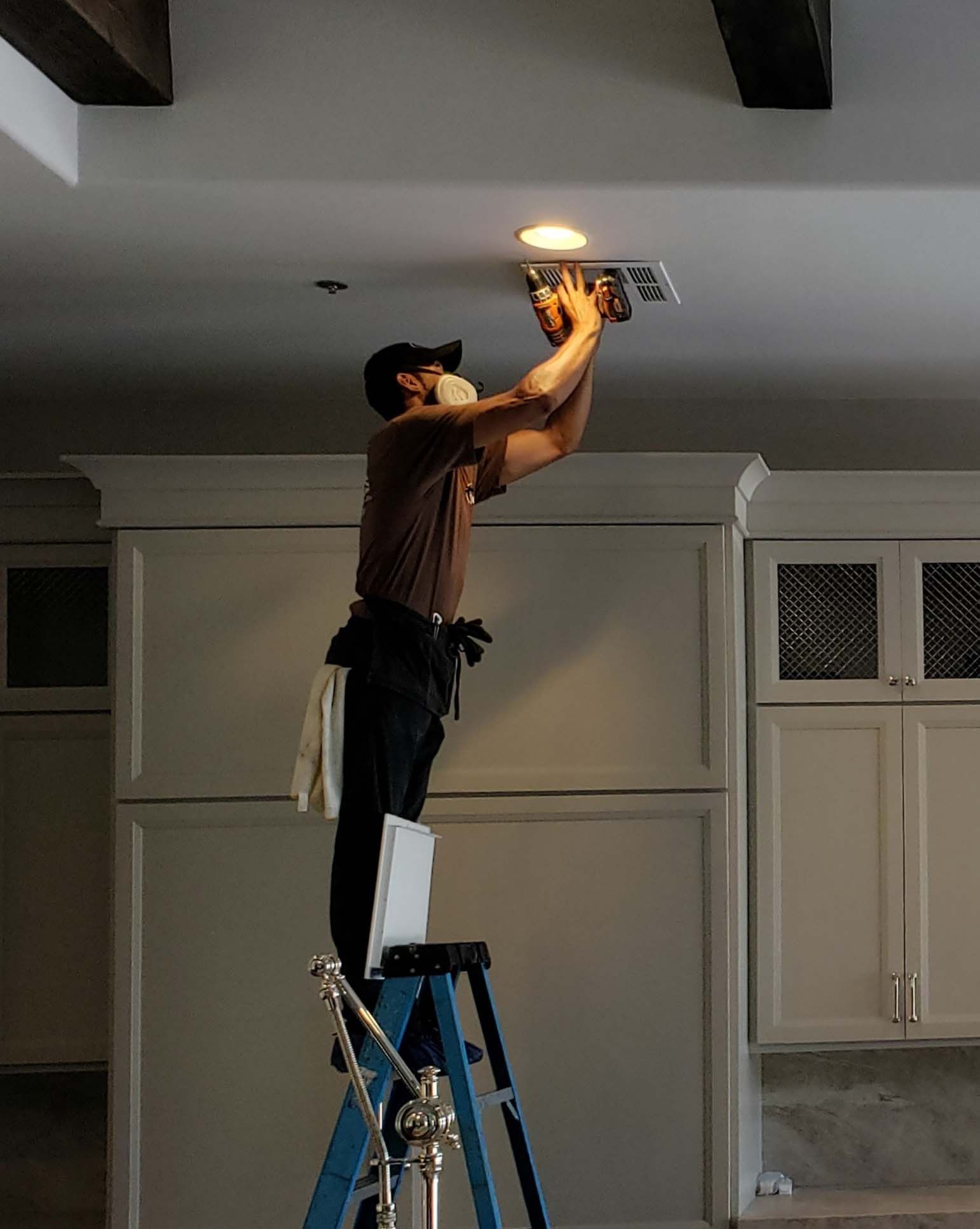 A man is standing on a ladder working on the ceiling