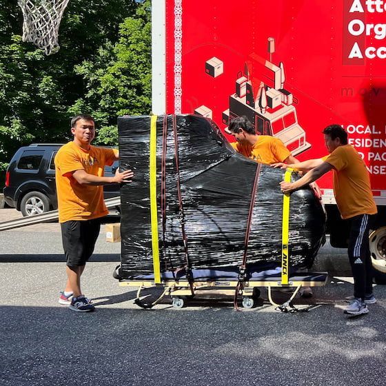 A man in a yellow shirt is pushing a piano on a cart