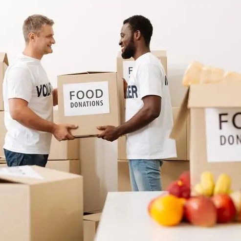Two men are holding boxes of food donations and talking to each other.