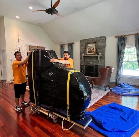 Two men are moving a piano in a living room