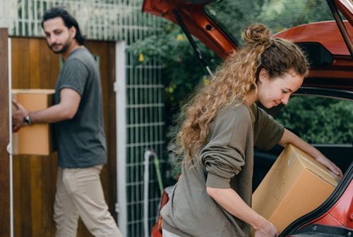 A man and a woman are loading boxes into the back of a car.