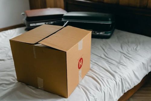 A cardboard box is sitting on a bed next to a suitcase.