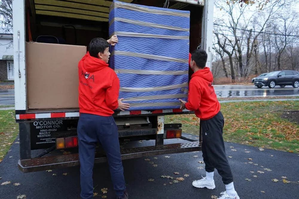 Two men are loading a blue mattress into a truck.