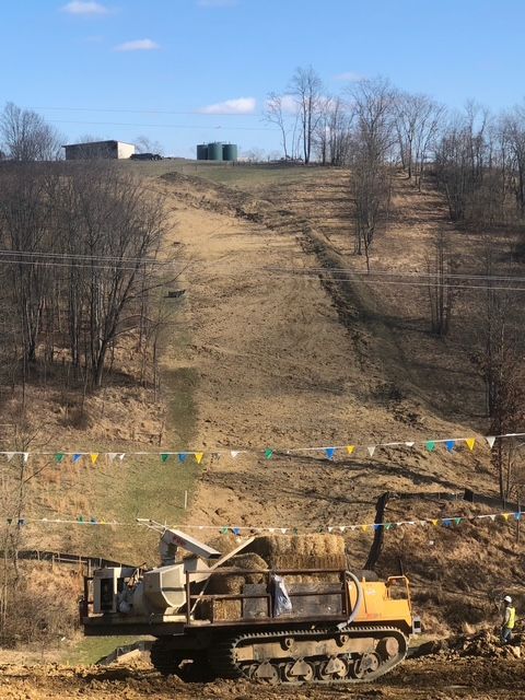 A yellow dump truck is driving down a dirt road.