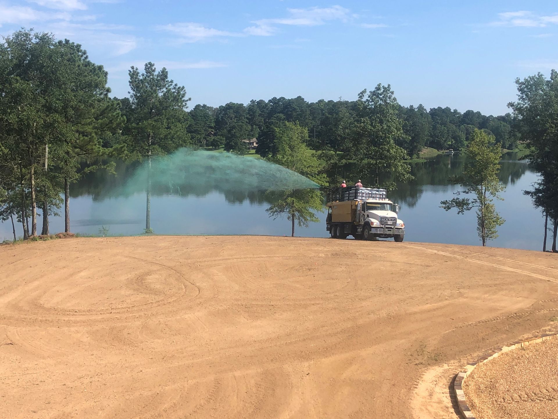 A truck is spraying water on a dirt road near a lake.