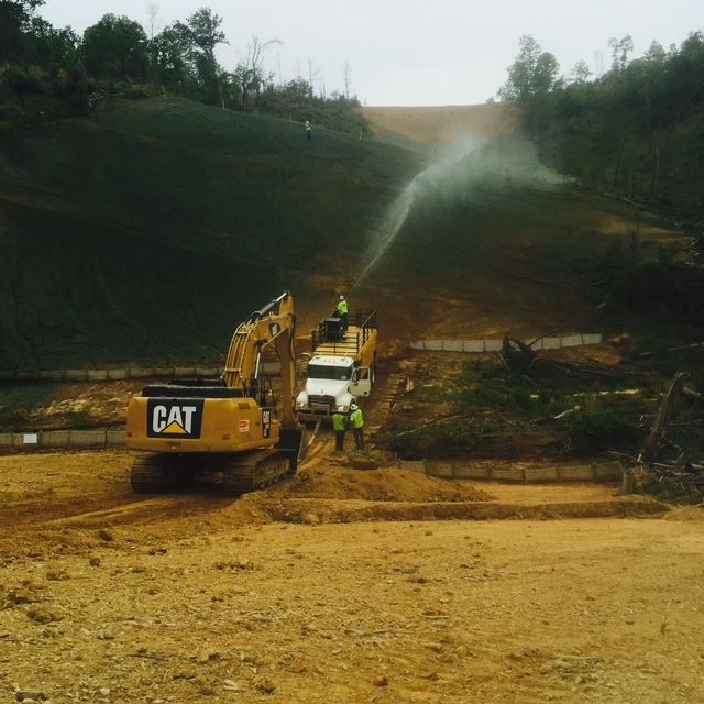 A cat excavator is spraying water on a dirt road