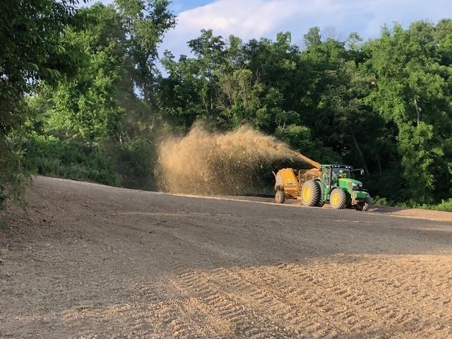A green tractor is driving down a dirt road.