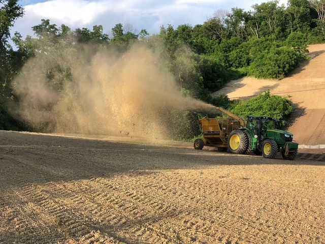 A green tractor is blowing dust in a field.