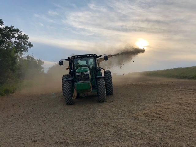A green tractor is spraying fertilizer on a dirt road.