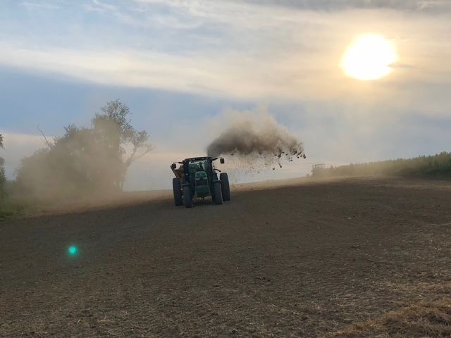 A tractor is plowing a field with smoke coming out of it.