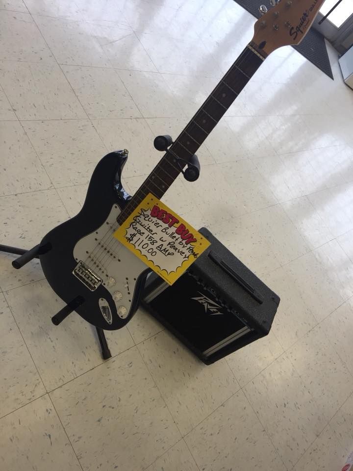 Black electric guitar and amplifier on a stand, for sale with a price tag on the body.