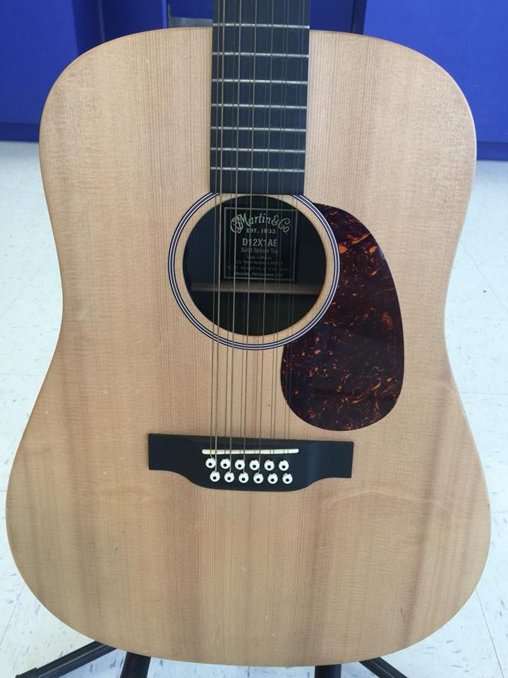 Acoustic 12-string guitar with a wooden body, brown pickguard, and a black bridge.