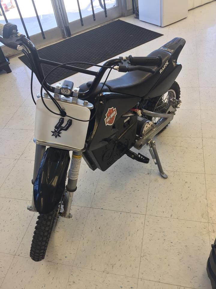 Black and silver electric dirt bike indoors, with a white front panel and Spurs logo.