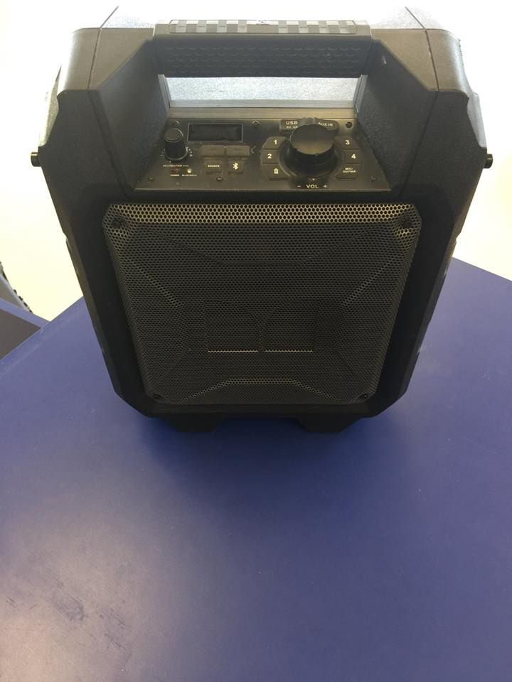 Black portable speaker with a handle on a blue surface.