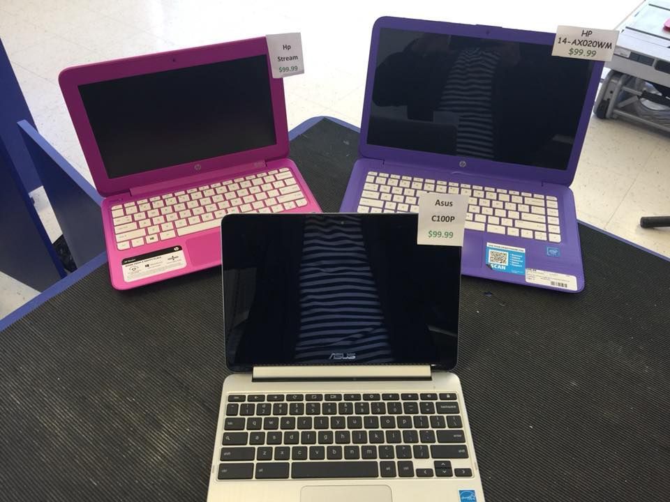 Three laptops displayed on a counter: pink, purple, and silver. Each has a price tag.