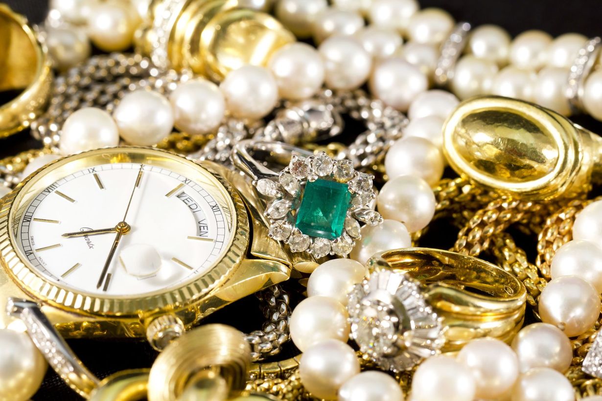 Pile of gold and silver jewelry on a black background, including chains, coins, and rings.