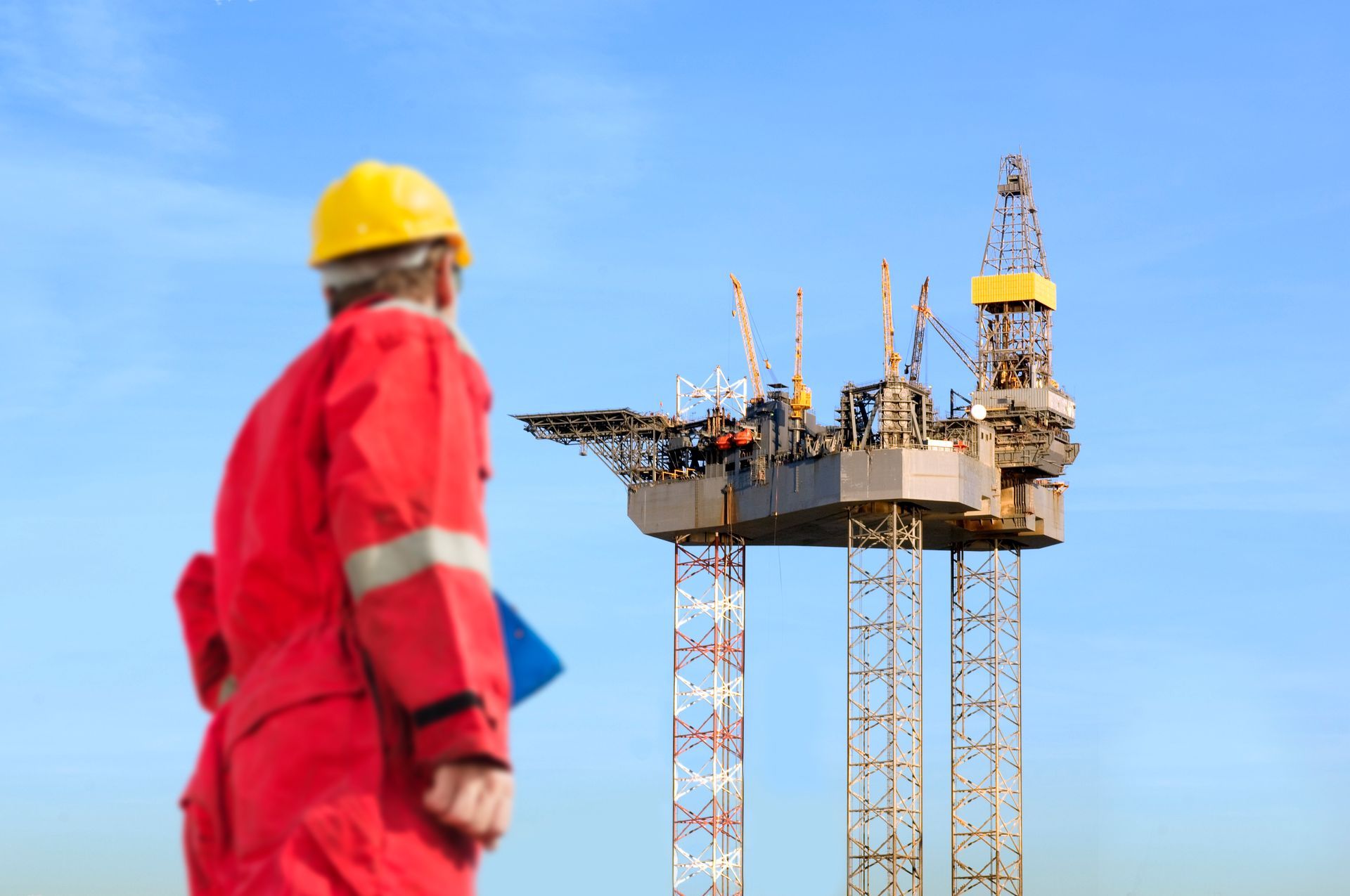 A man in a hard hat is standing in front of an oil rig.
