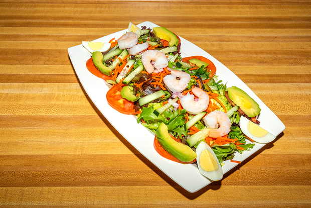 Platter of shrimp salad with avocado, cherry tomatoes, and lemon wedges on a wooden table