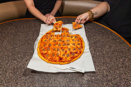 Hands lifting a slice from a heart-shaped pepperoni pizza on a table