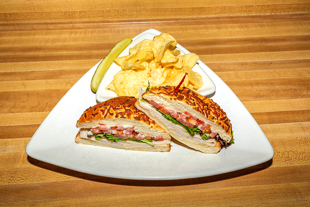 Sandwich halves with chips and a pickle on a white plate on a wooden table