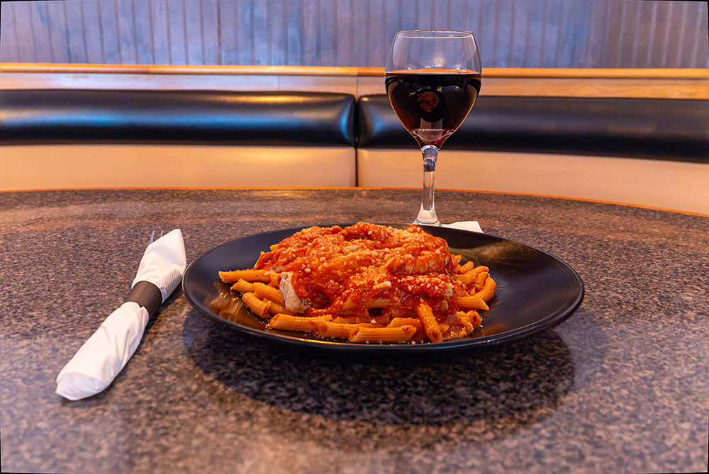 Plate of pasta with red sauce on a table beside a glass of red wine and a rolled napkin