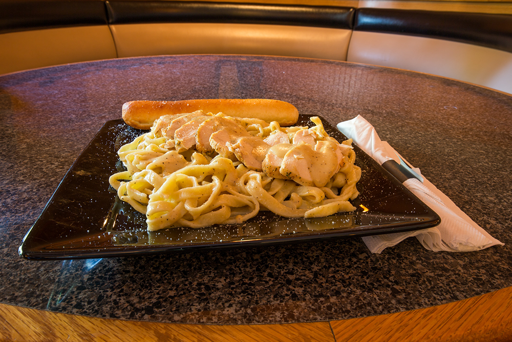 Pasta with creamy sauce and breadstick on a black plate in a restaurant booth