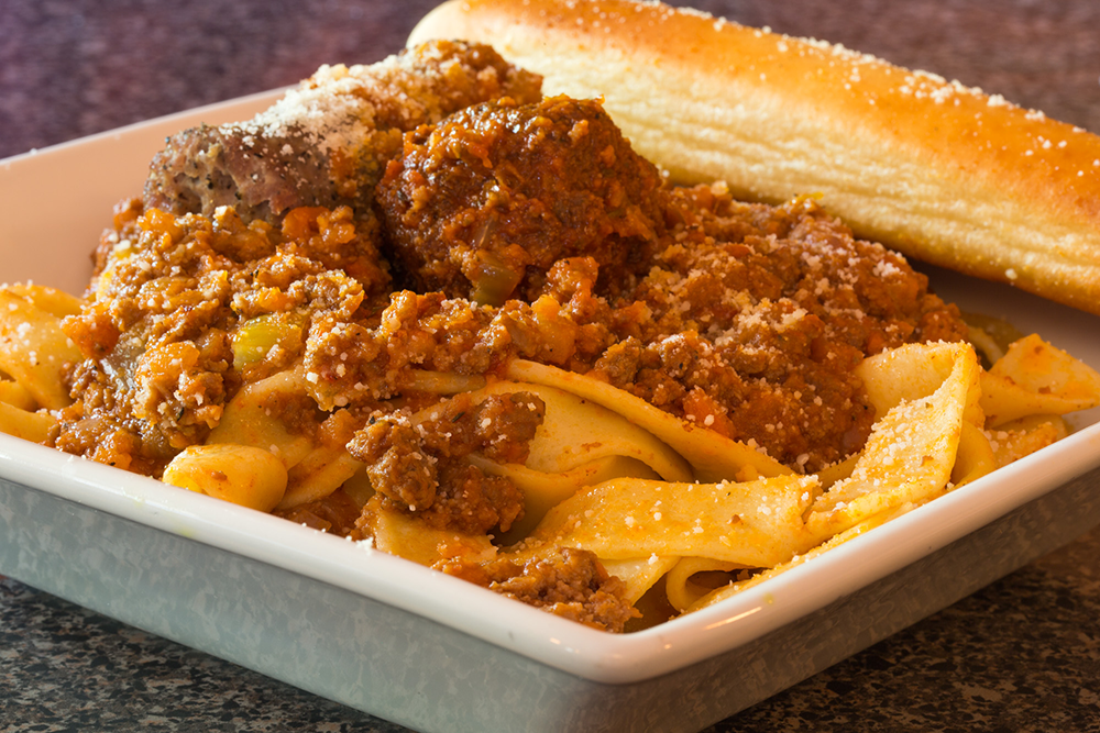Plate of pasta with meat sauce and garlic bread on a table